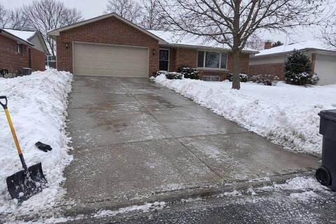 A cleared concrete driveway beside a single-story full-brick ranch house, snow banked along both edges and an attached two-car garage door closed