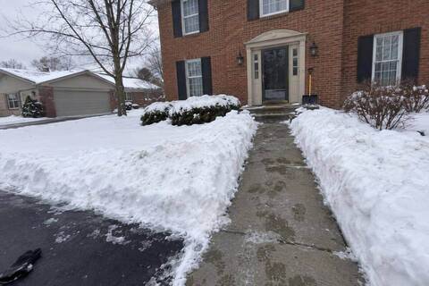 A shoveled walk from a driveway to the front steps of a colonial house, snow walls on either side and a shovel leaning by the door